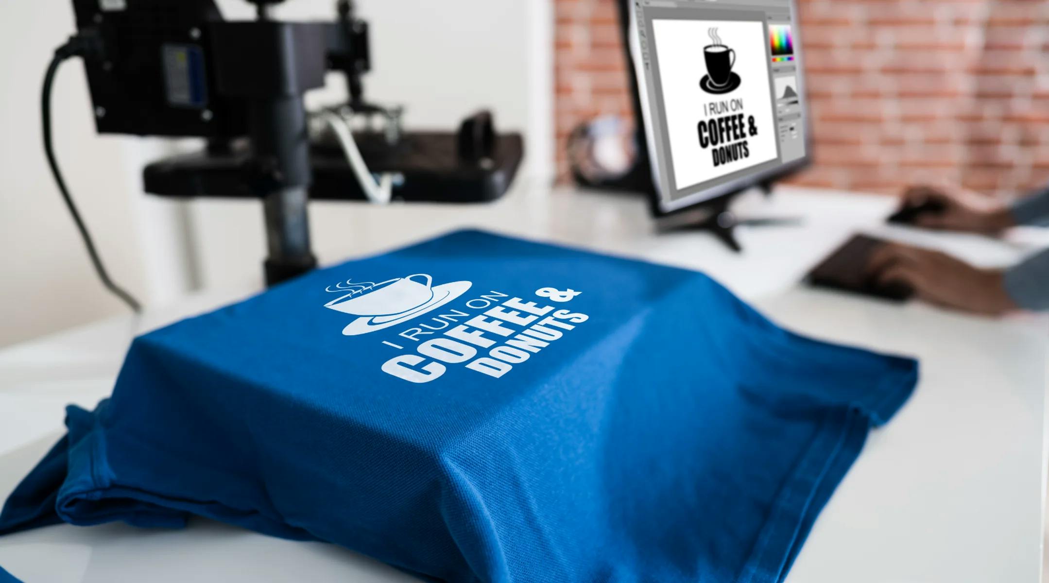 Blå t-skjorte med teksten "I run on coffe & donuts" som ligger på en varmepresse