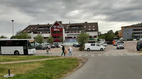 En buss til venstre, en familie på tre går over et gangfelt. Andebu sentrumsbygg i bakgrunnen.