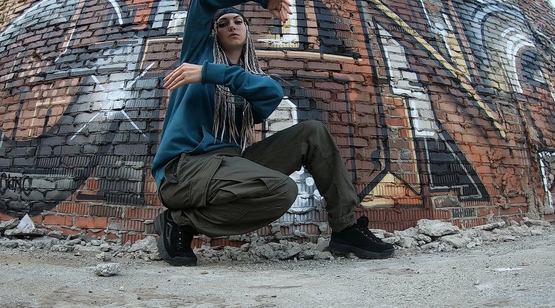 Kvinne som poserer i hip hop-stil foran en tagget murvegg. Foto