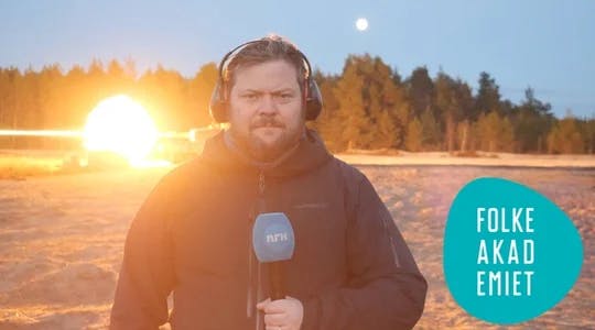 En mann står ute i et snødekt landskap med en NRK-mikrofon i hånda og headset på hodet.