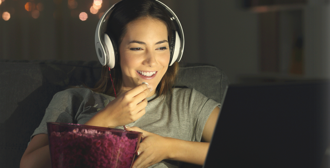 Kvinne med headset som ser på film og spiser popcorn. Foto.